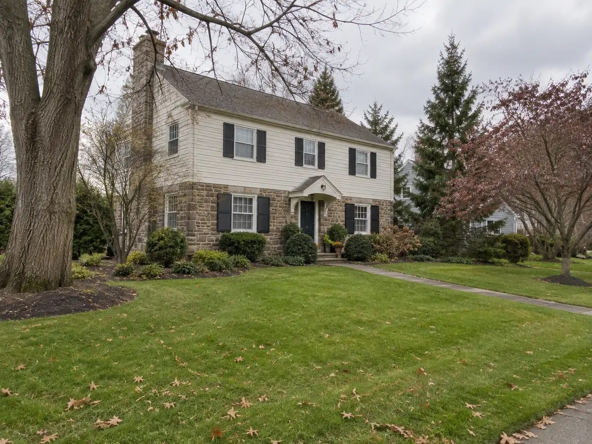 Stone-and-siding house with lawn, mature trees and foundation planting beds.